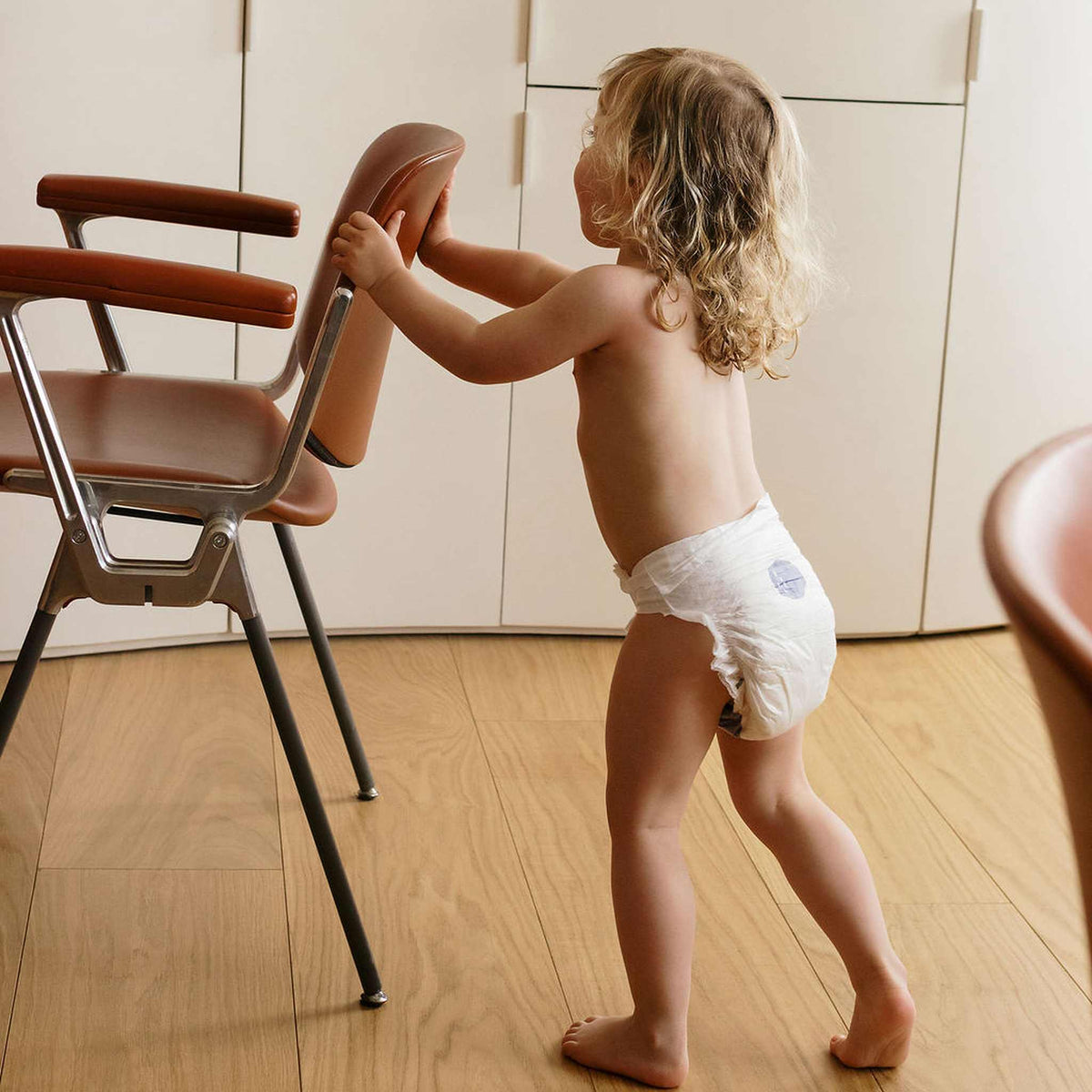 Enfant en couche Biolane faisant ses premiers pas en s’appuyant sur une chaise
