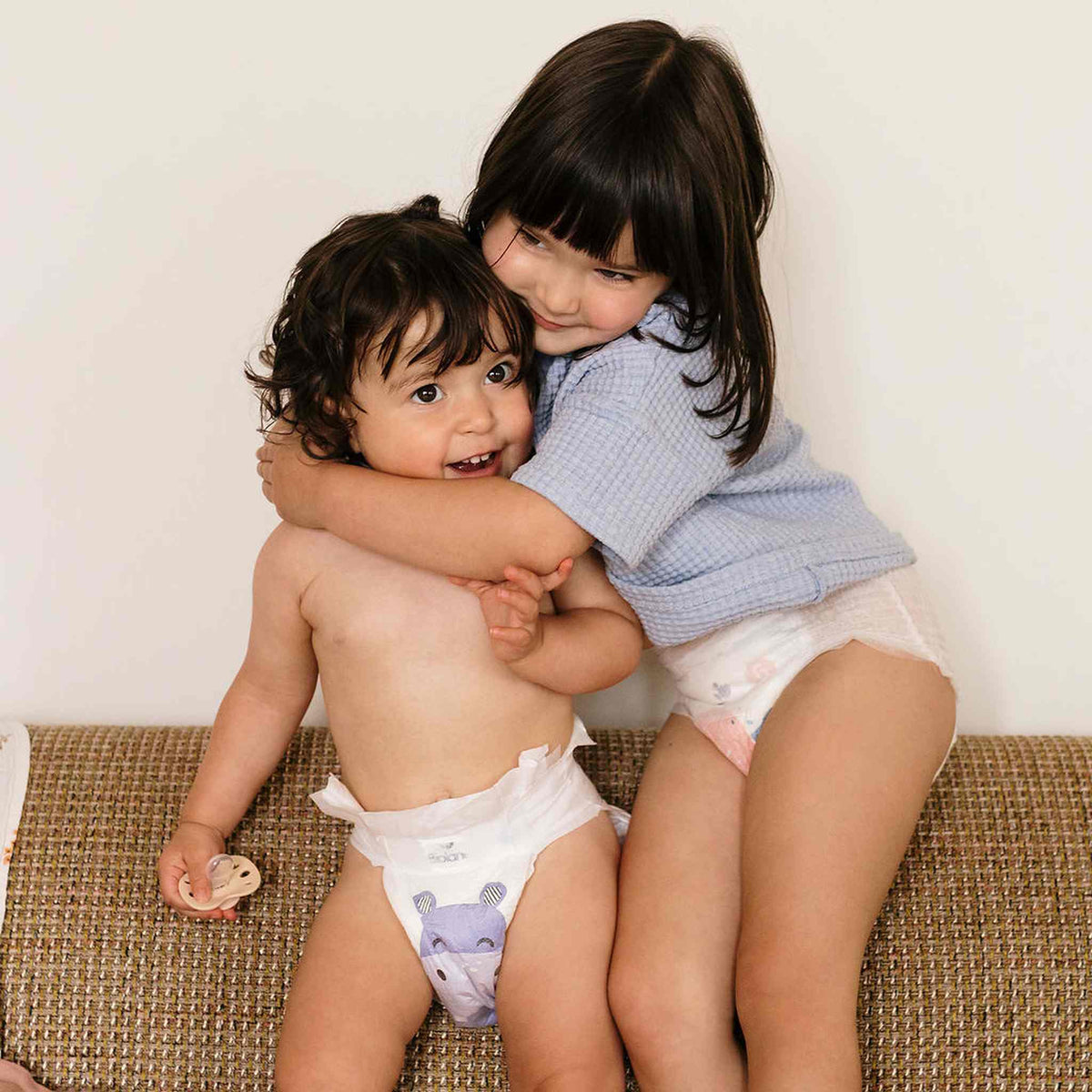 Deux enfants en couches Biolane à motif hippopotame se font un câlin