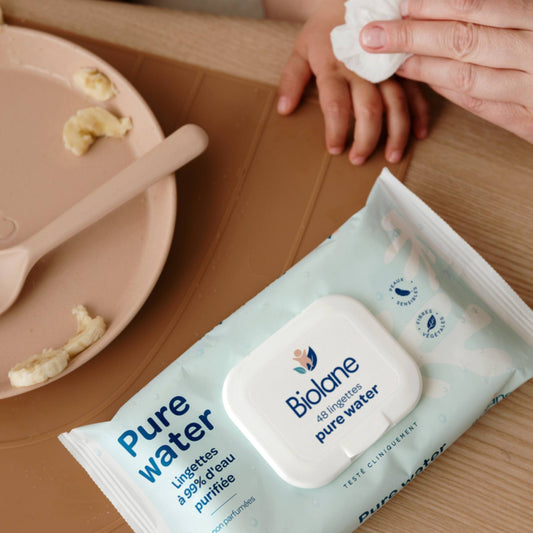 Les mains d’un bébé nettoyées avec une lingette Pure Water Biolane au moment du repas