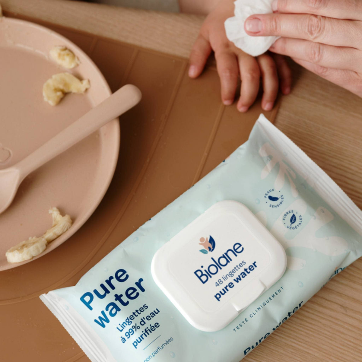 Les mains d’un bébé nettoyées avec une lingette Pure Water Biolane au moment du repas
