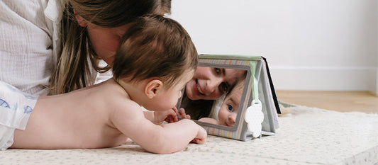 Un bébé joue avec sa maman et se regarde dans un miroir.