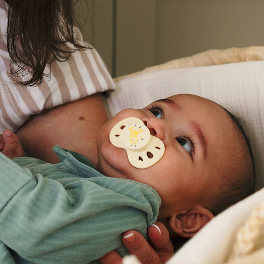 Un bébé avec une sucette Biolane allongé dans les bras de sa maman