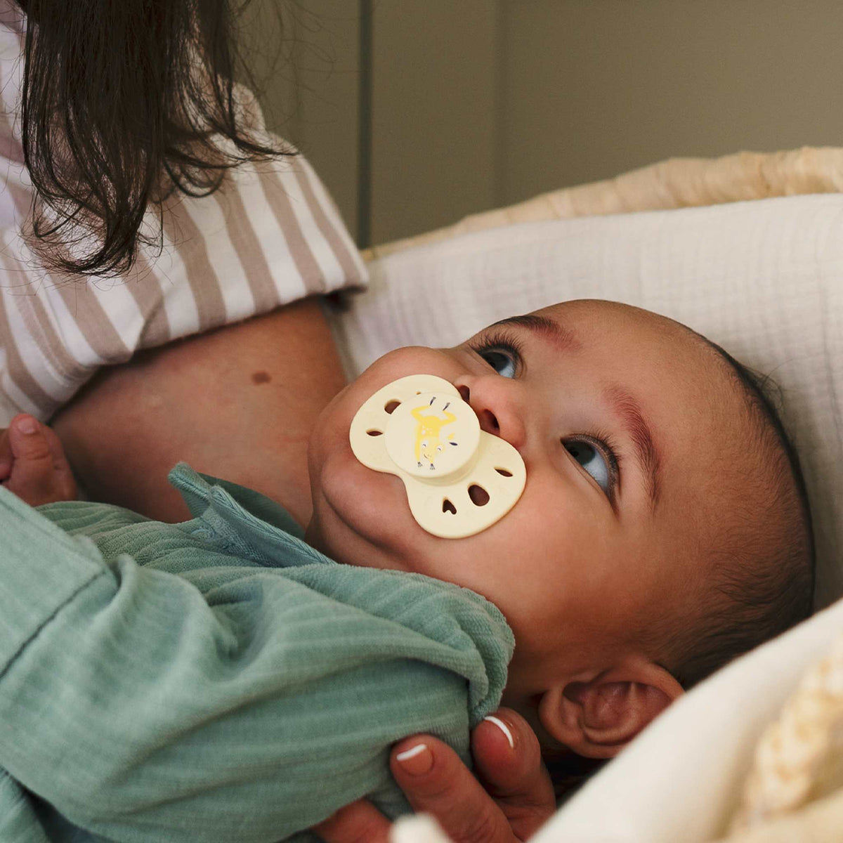 Un bébé avec une sucette Biolane allongé dans les bras de sa maman